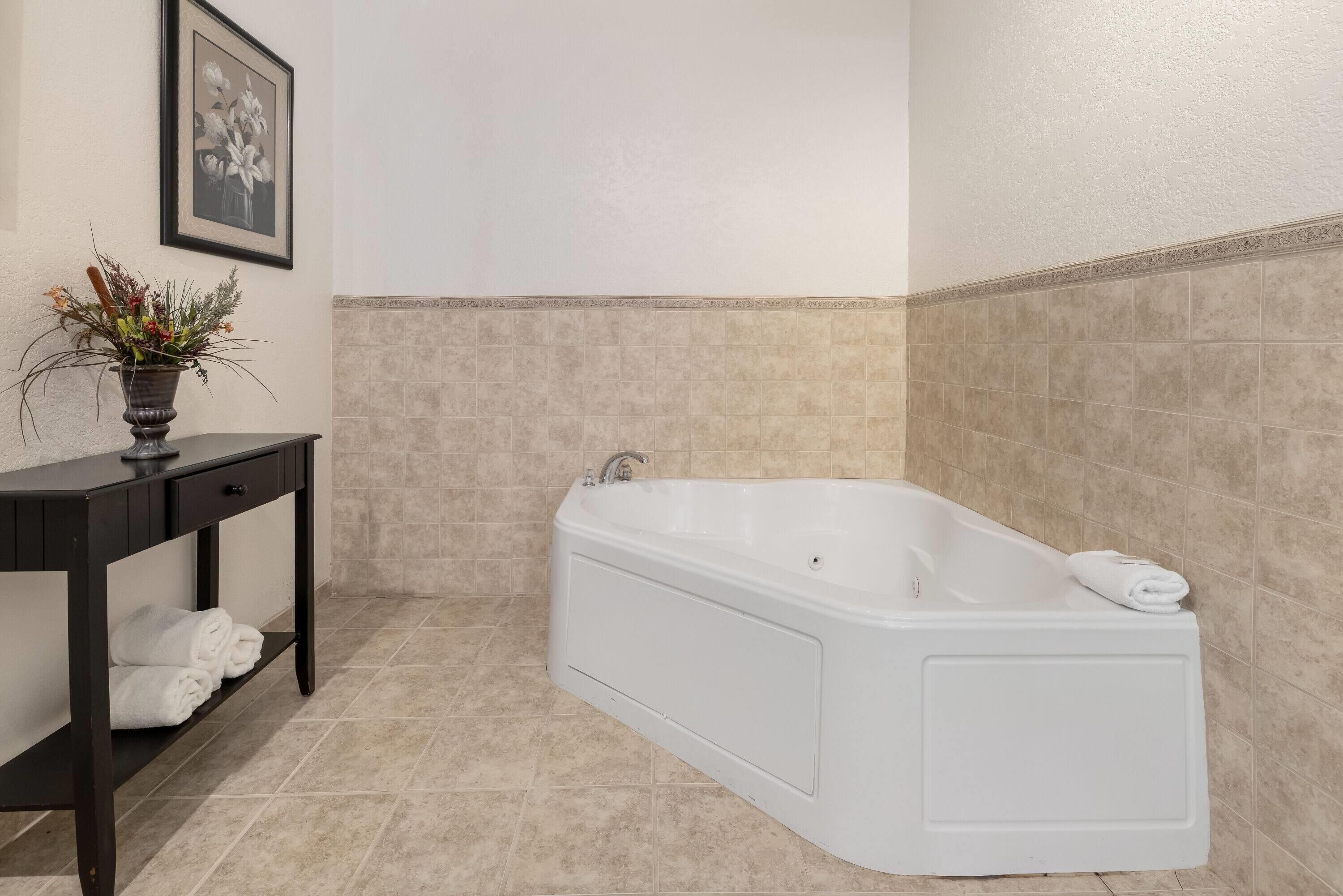 A modern bathroom with a freestanding bathtub, a dark wooden vanity with a vase of flowers, and a framed picture on the wall.