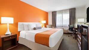 Ein Hotelzimmer mit einem großen Bett, zwei Nachttischen mit Lampen, einem Schreibtisch, einem Sessel, einem Fernseher und einem Fenster mit Vorhängen.