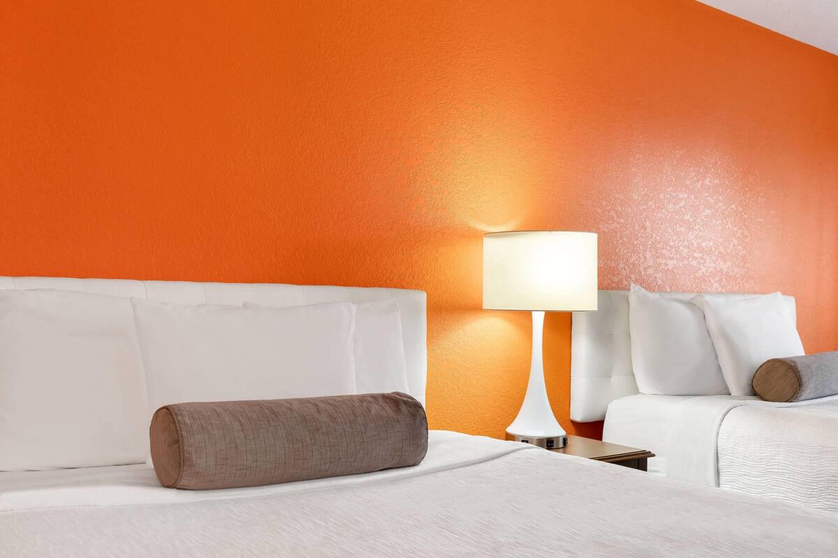Ein Hotelzimmer mit einem weißen Bett, einem braunen Kopfkissen und einer orangefarbenen Wand.