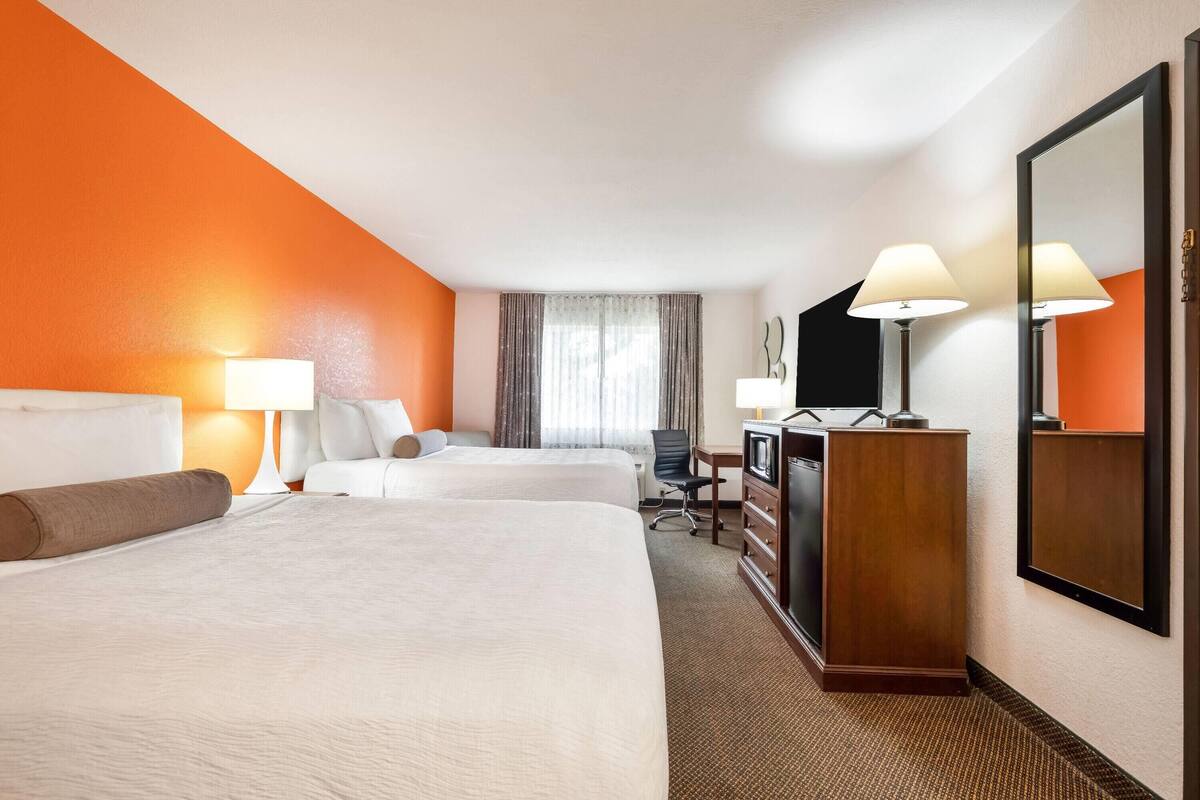 Ein Hotelzimmer mit zwei Betten, einem Schreibtisch, einem Stuhl, einer Kommode und einem großen Spiegel.