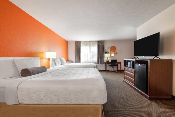 A hotel room with two beds, a TV, a desk with a lamp, and a minibar.
