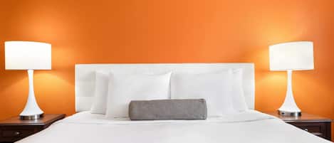 A hotel room with a large bed, two bedside lamps, and an orange wall.