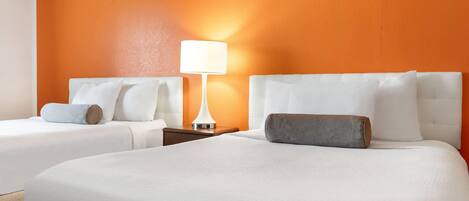 A hotel room with two beds, a nightstand, and a lamp.