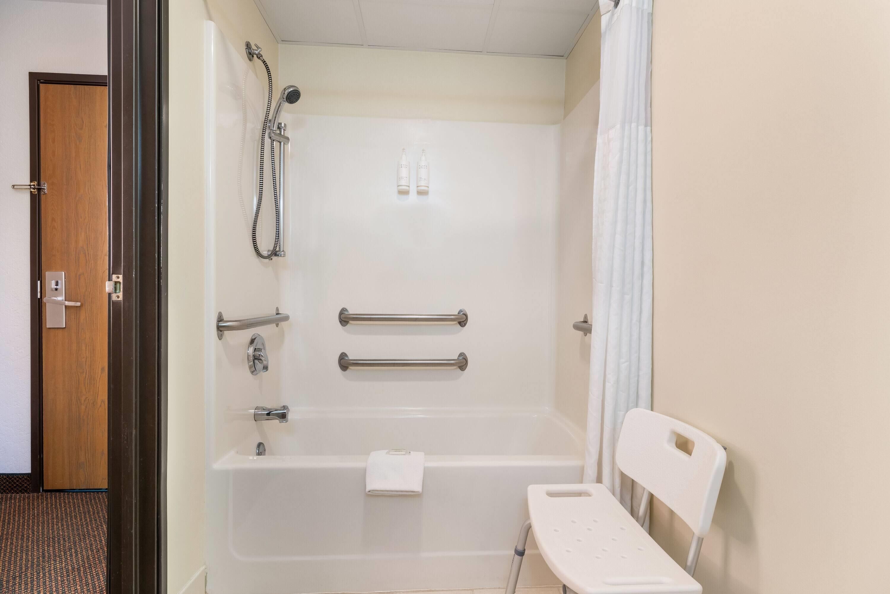 Ein Badezimmer mit einer Badewanne, Haltegriffen, einer Duschbrause und einem Handtuchhalter.