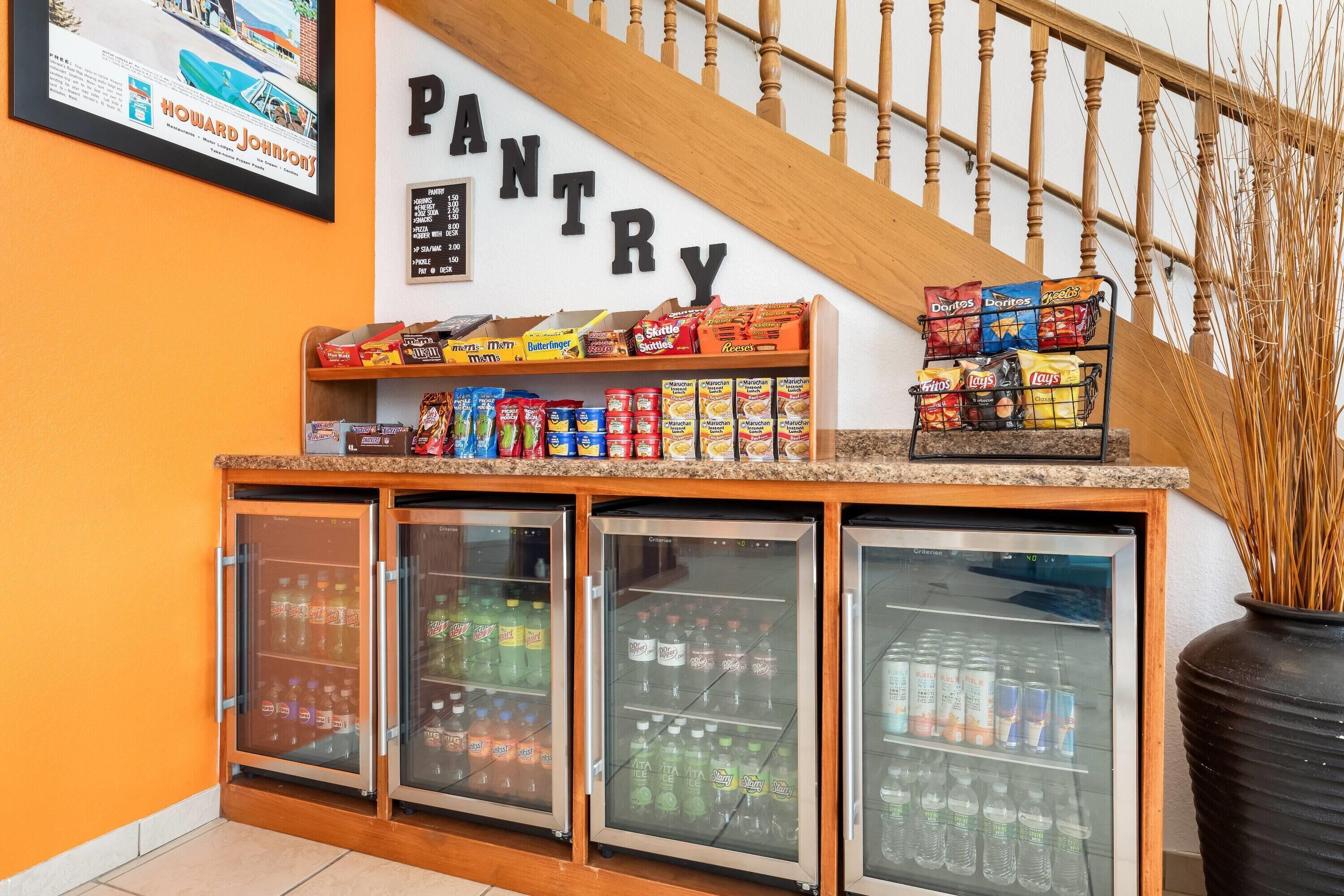A pantry area with shelves stocked with snacks and a refrigerator with beverages.