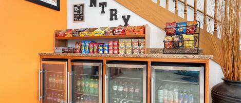 A pantry area with shelves stocked with snacks and a refrigerator with beverages.