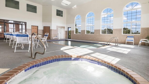 Ein Poolbereich mit Whirlpool, Liegestühlen und Blick ins Freie durch große Fenster.