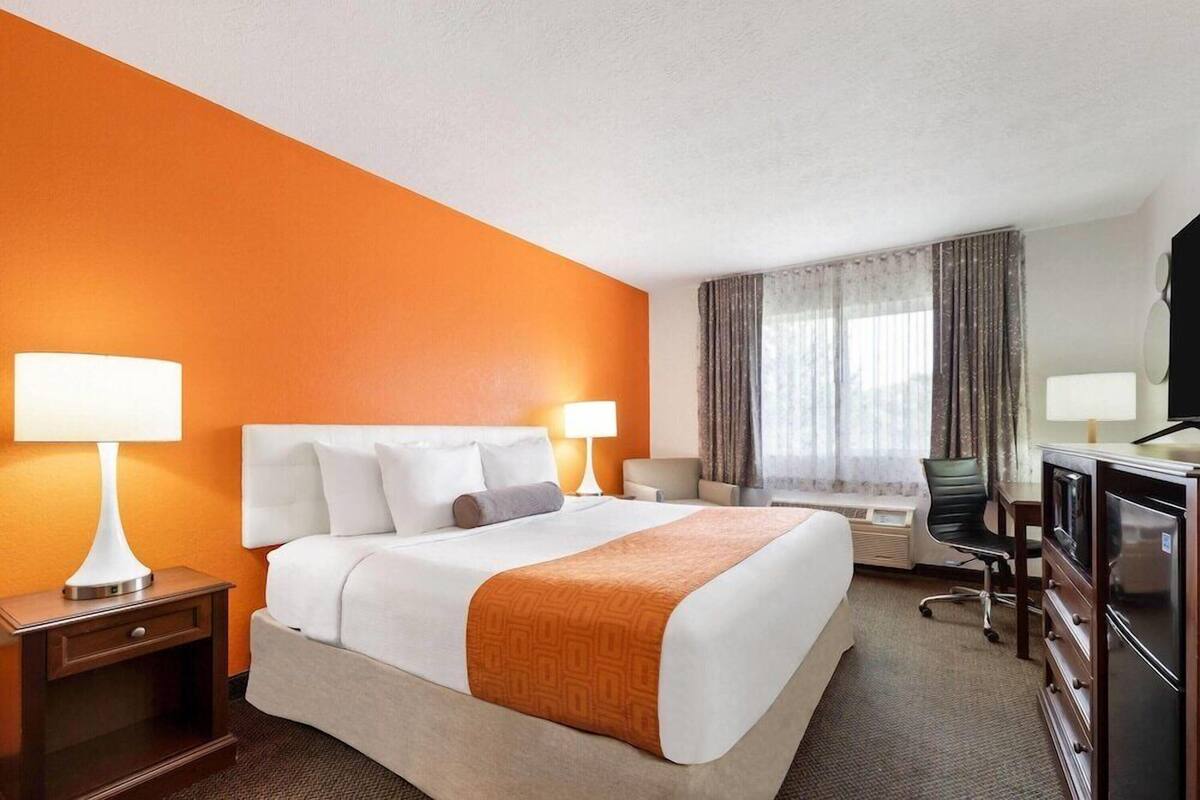 Ein Hotelzimmer mit einem Bett, Nachttischlampen, einem Schreibtisch, einem Stuhl, einem Fernseher und einem Fenster mit Vorh ängen.