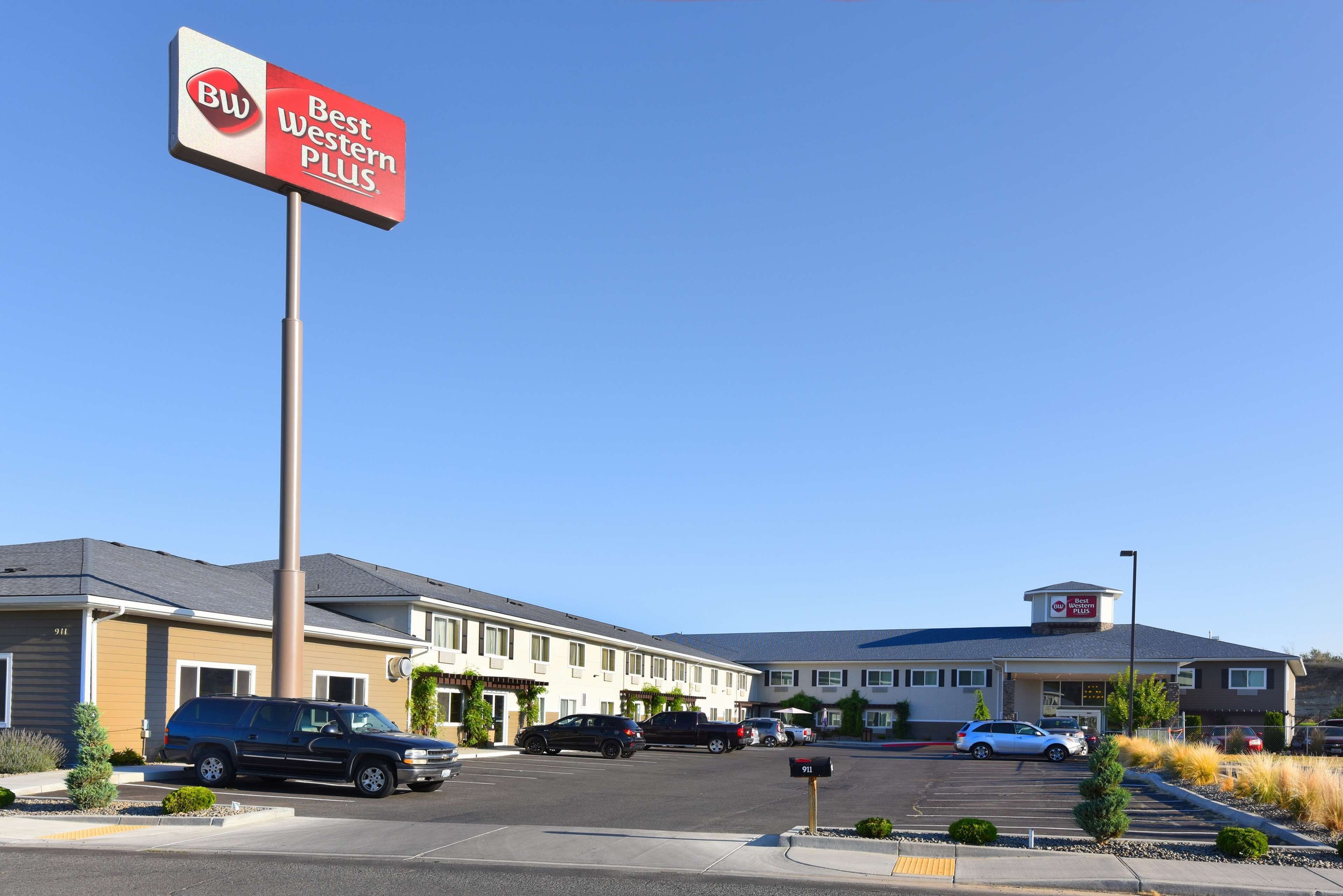 Un hotel Best Western Plus con estacionamiento, varios automóviles y un cielo azul despejado.