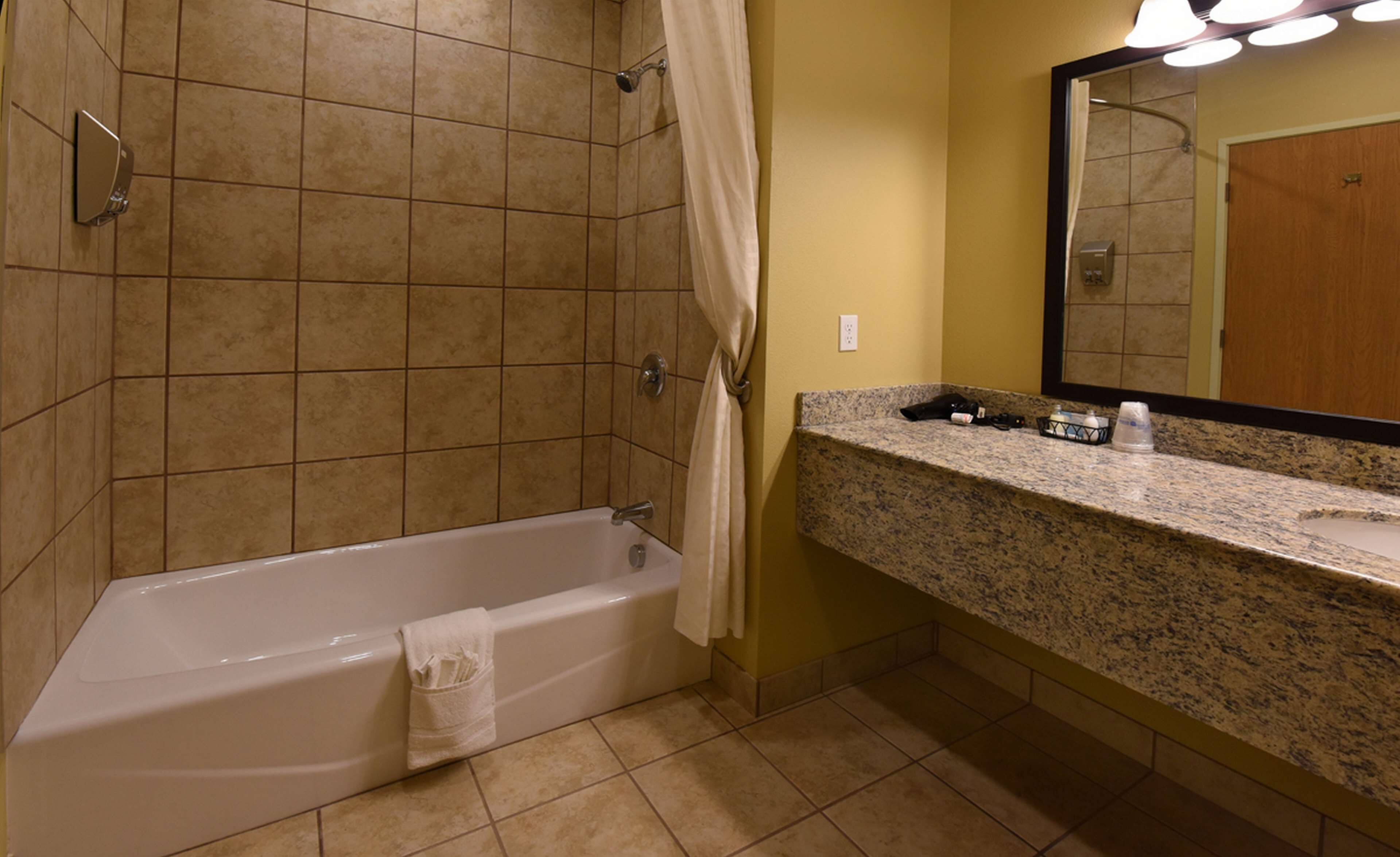 Une salle de bain équipée d’une baignoire, d’une douche, d’un plan de toilette en granit et d’un miroir.