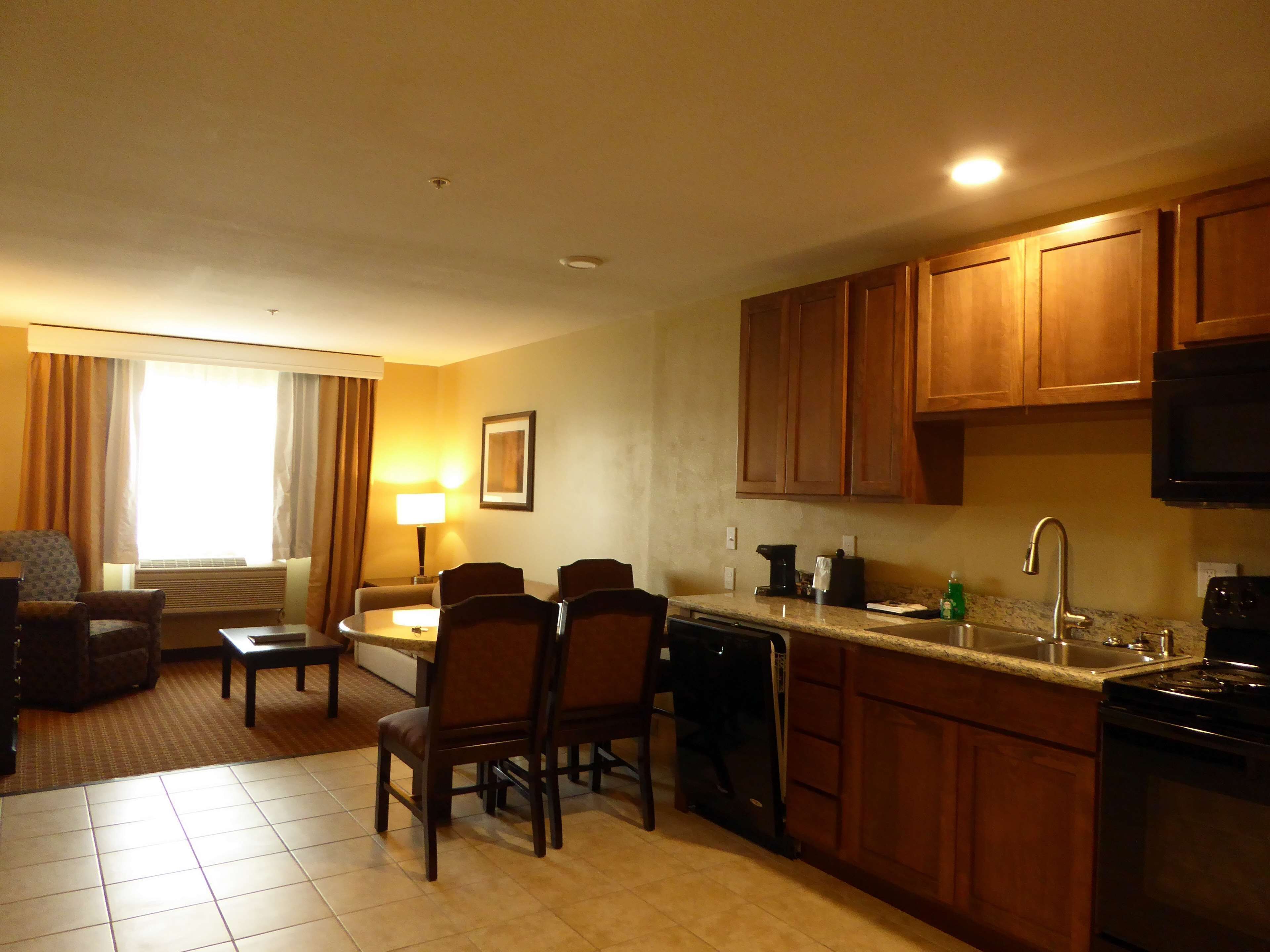 A compact hotel room with a dining area, kitchenette, and a seating area with a lamp.