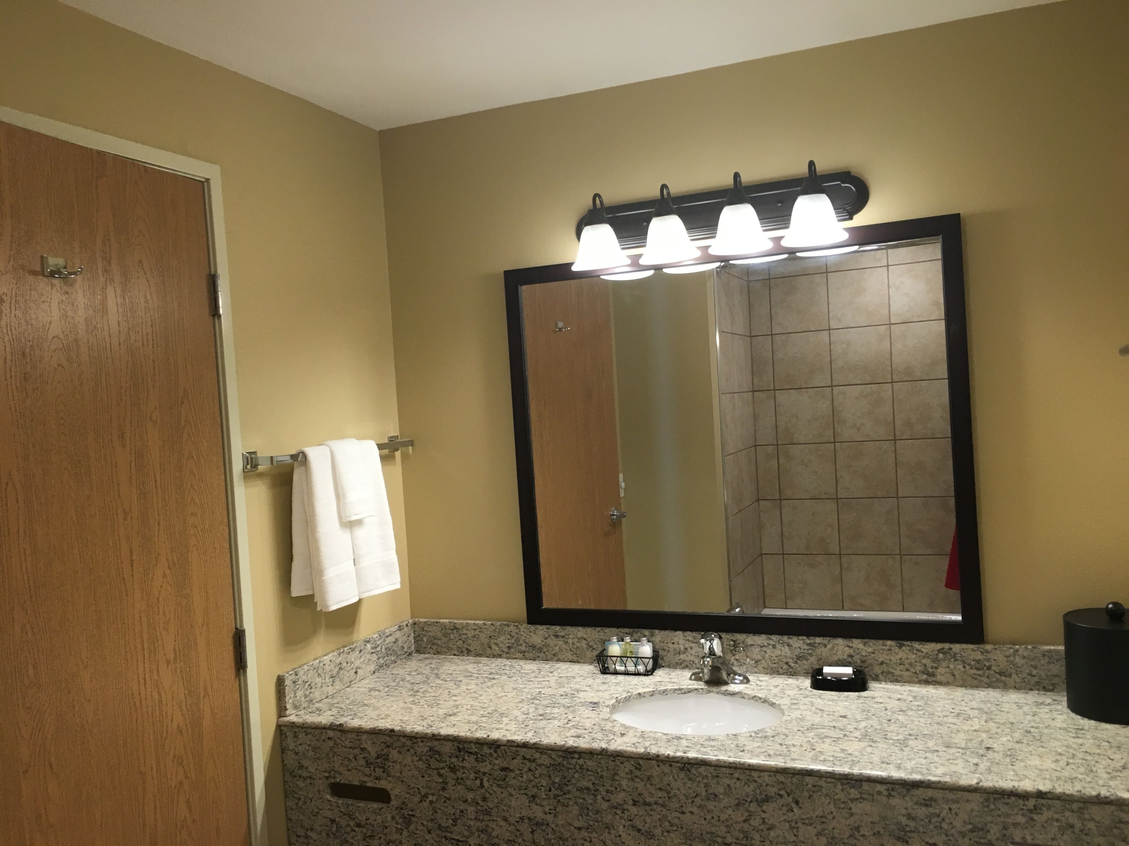 A bathroom with a granite countertop, a sink, a mirror with lights, and a towel hanging on a rack.