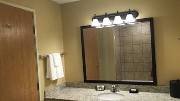 A bathroom with a granite countertop, a sink, a mirror with lights, and a towel hanging on a rack.
