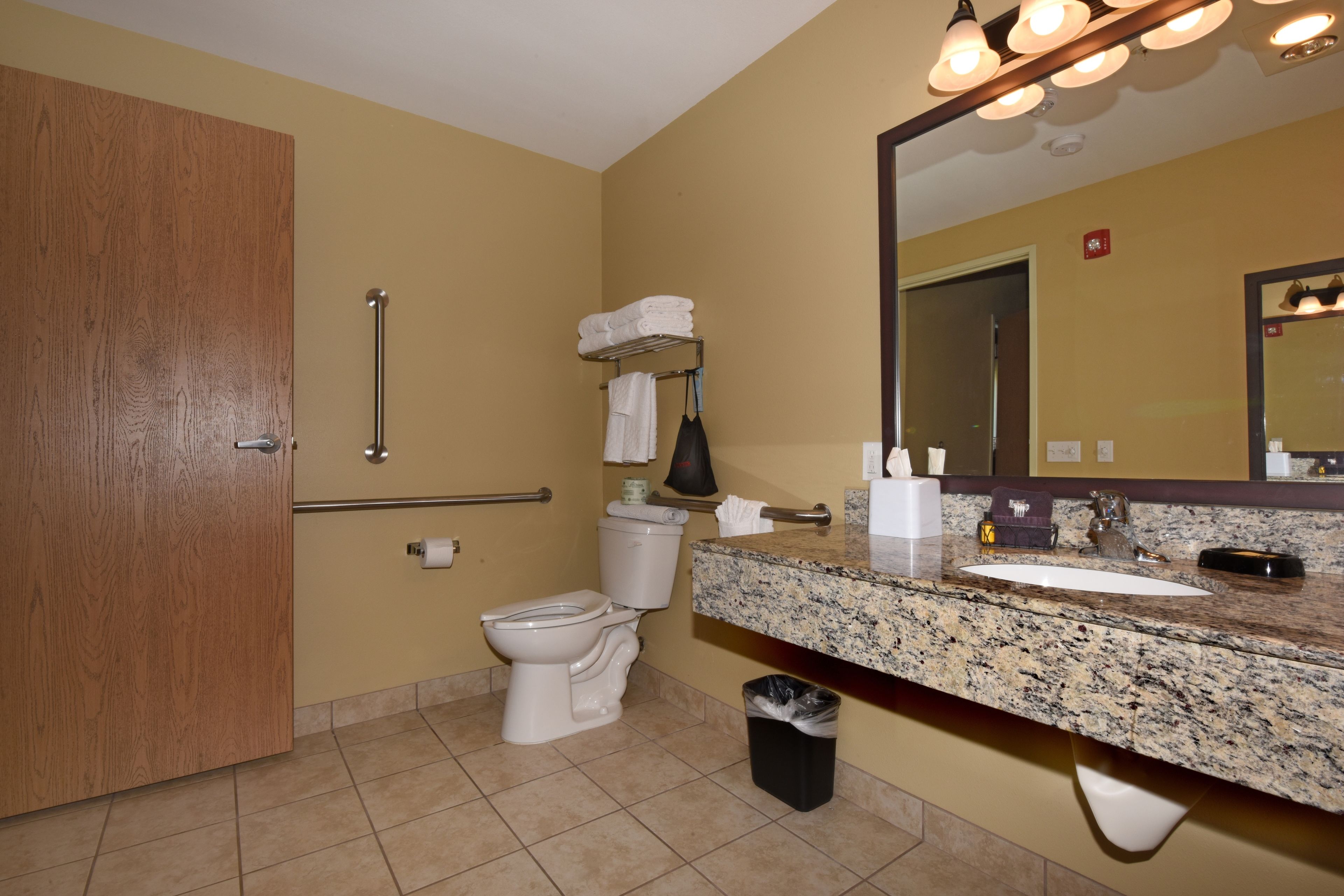 A bathroom with a toilet, sink, mirror, towel rack, and trash bin.
