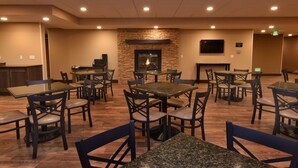A dining area with tables and chairs, a stone fireplace, and a flat-screen TV mounted on the wall. - Best Western Plus Vintage Valley Inn (Zillah)