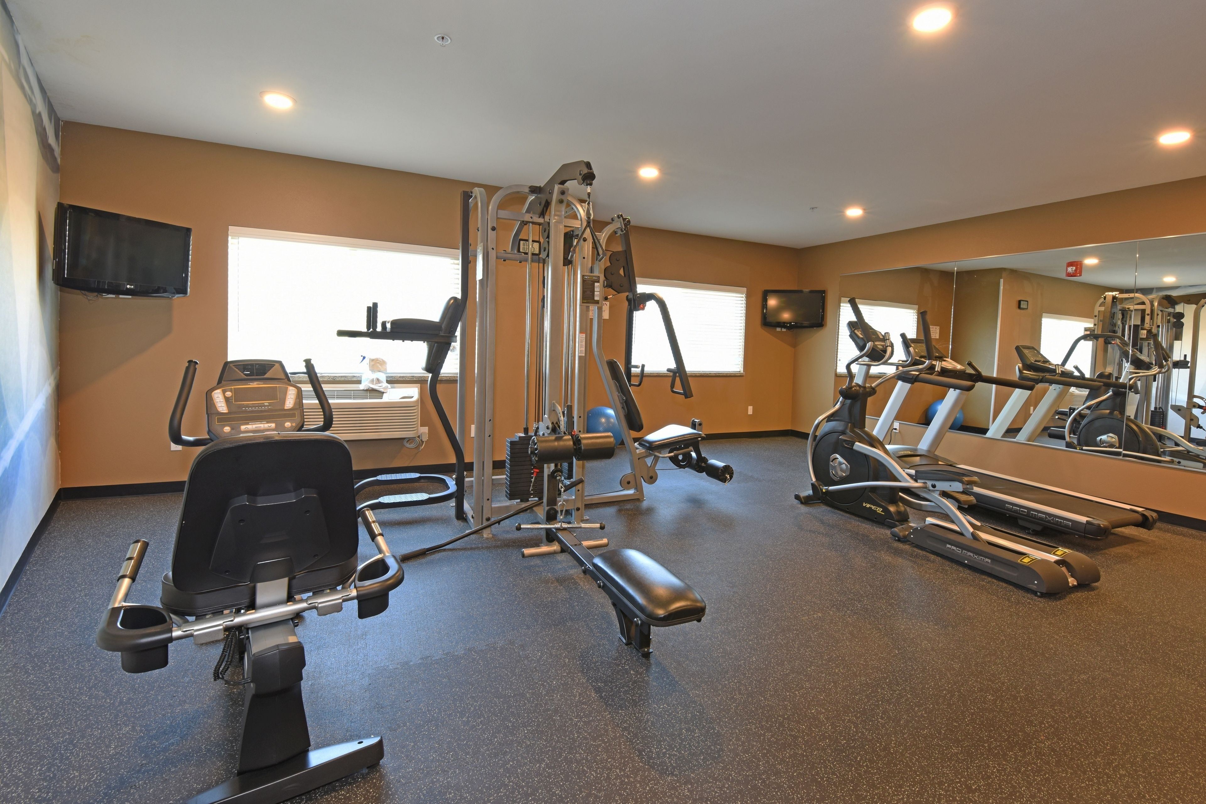 Un gimnasio con máquinas de cardio, equipo de pesas y un espejo grande.