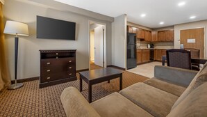 A hotel room with a living area, a flat-screen TV, a dark wooden dresser, a small table, and a sofa. - Best Western Plus Vintage Valley Inn (Zillah)