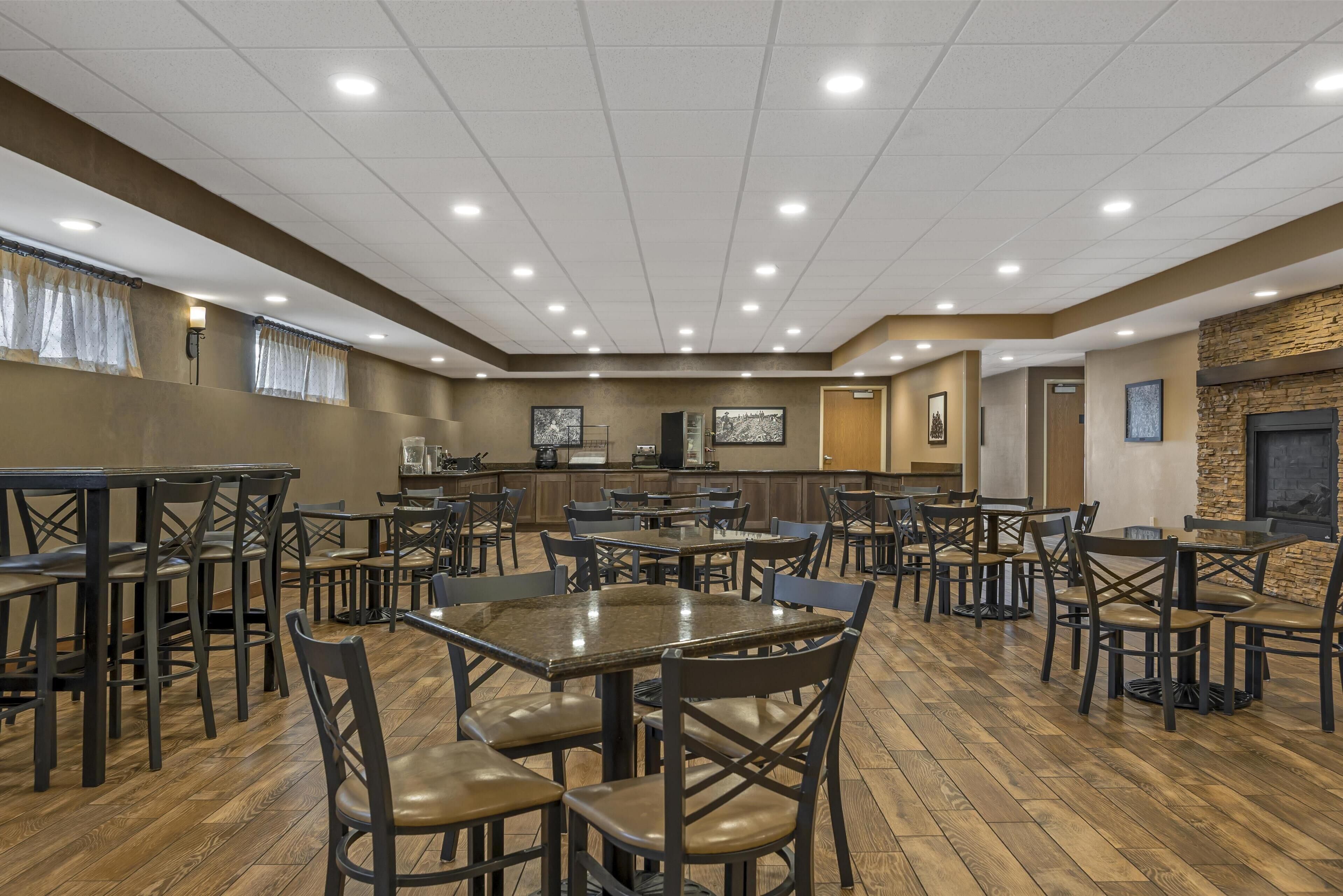 A spacious dining area with multiple tables and chairs, a kitchen in the background, and a stone fireplace.