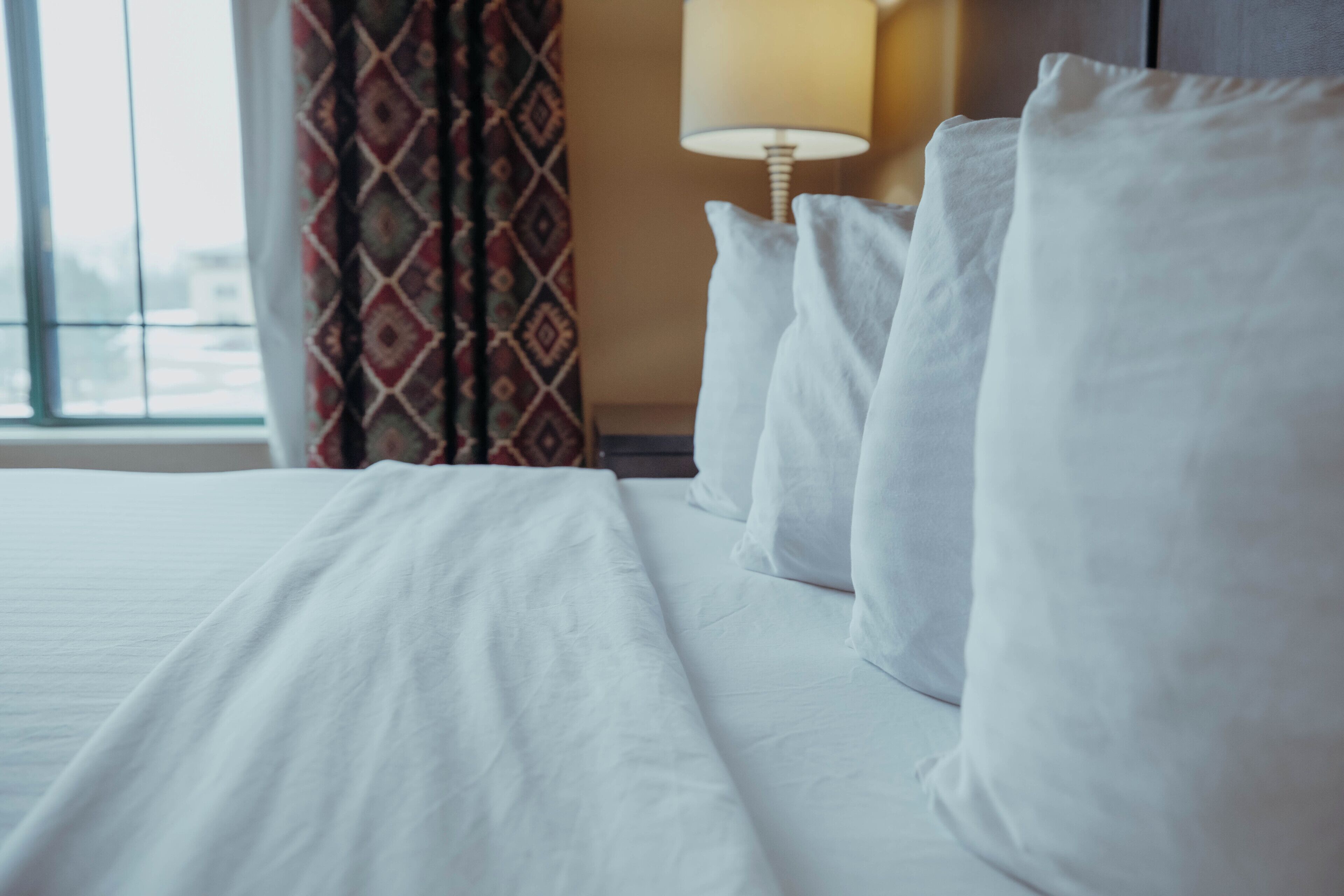 Une chambre d’hôtel avec un lit bien fait, du linge de lit blanc, une lampe sur la table de chevet et une fenêtre avec des rideaux.
