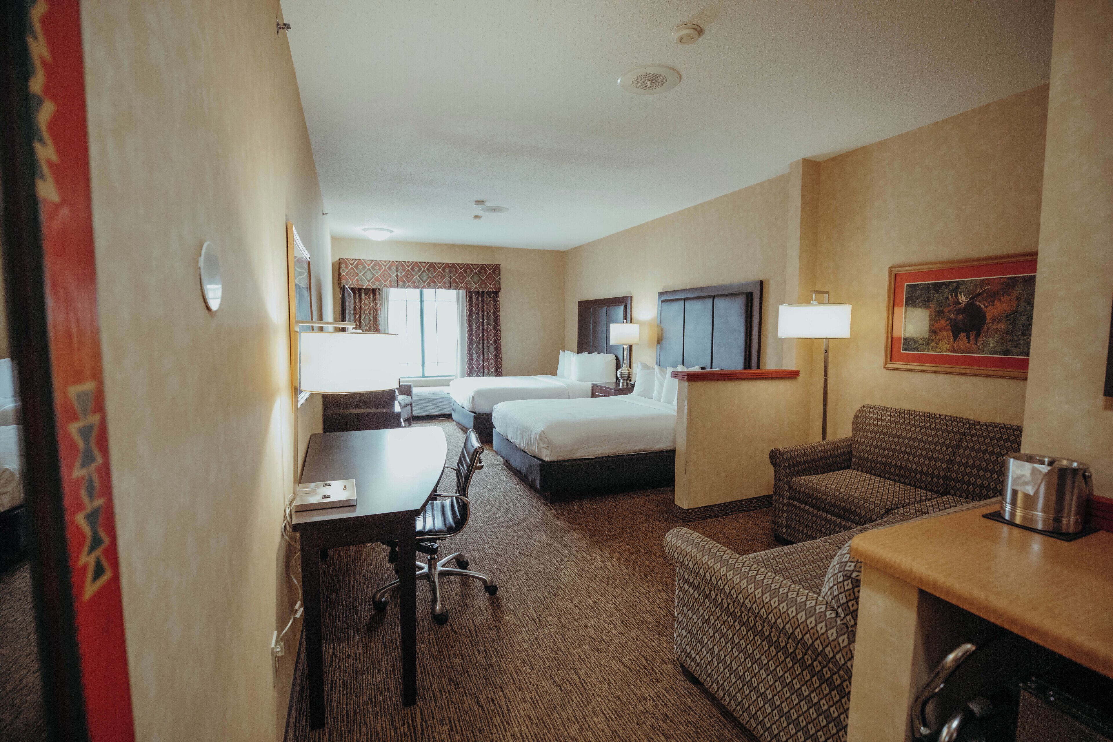 A hotel room with a bed, desk, chair, and a kitchenette.