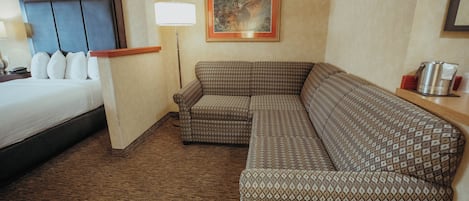 A hotel room with a bed, a patterned sofa, a lamp, and a framed picture on the wall.