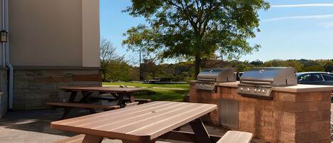 An outdoor patio with picnic tables and a barbecue grill.