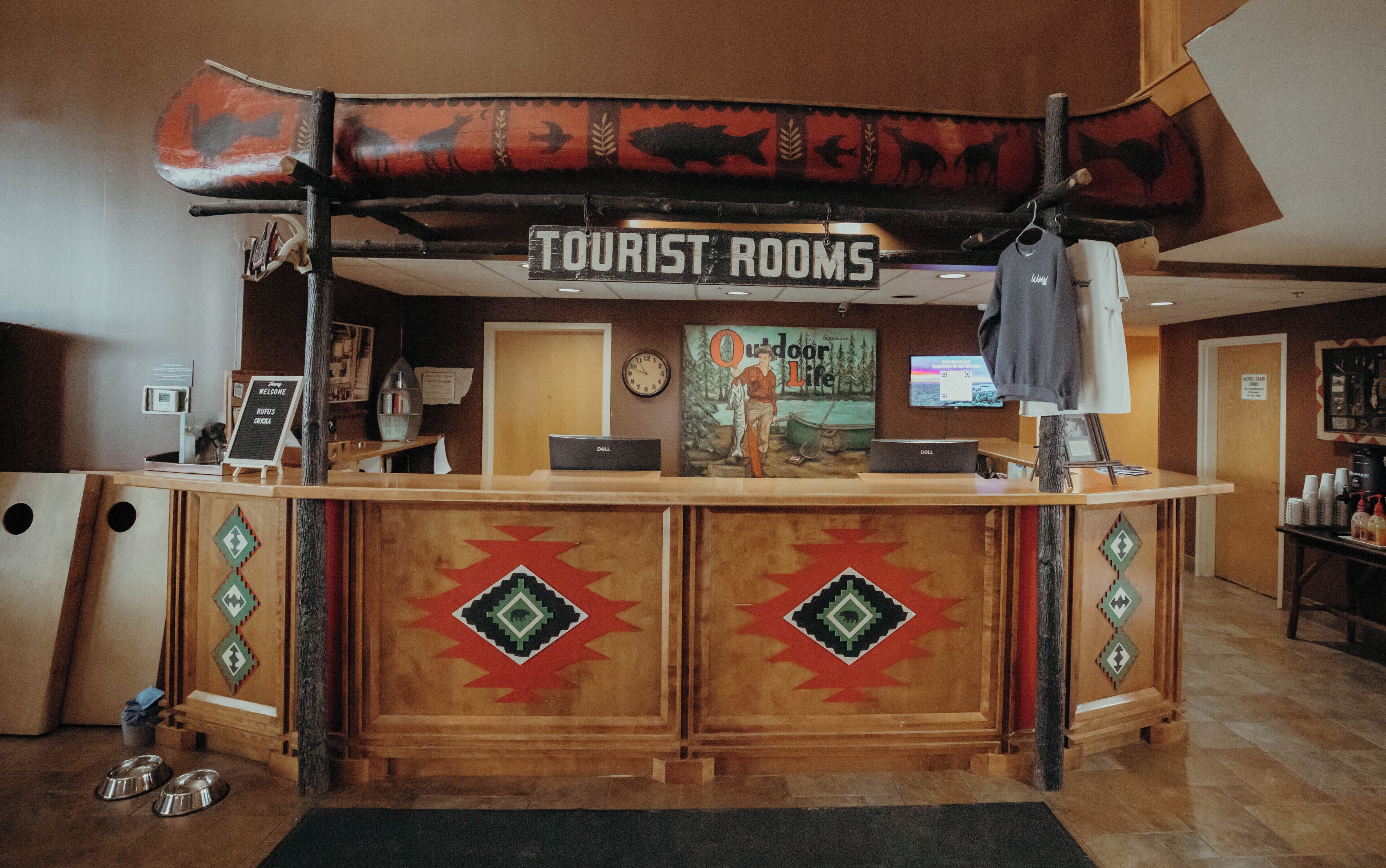 A reception desk with a sign reading "Tourist Rooms," a clock, a Dell computer, and a poster of a man fishing.