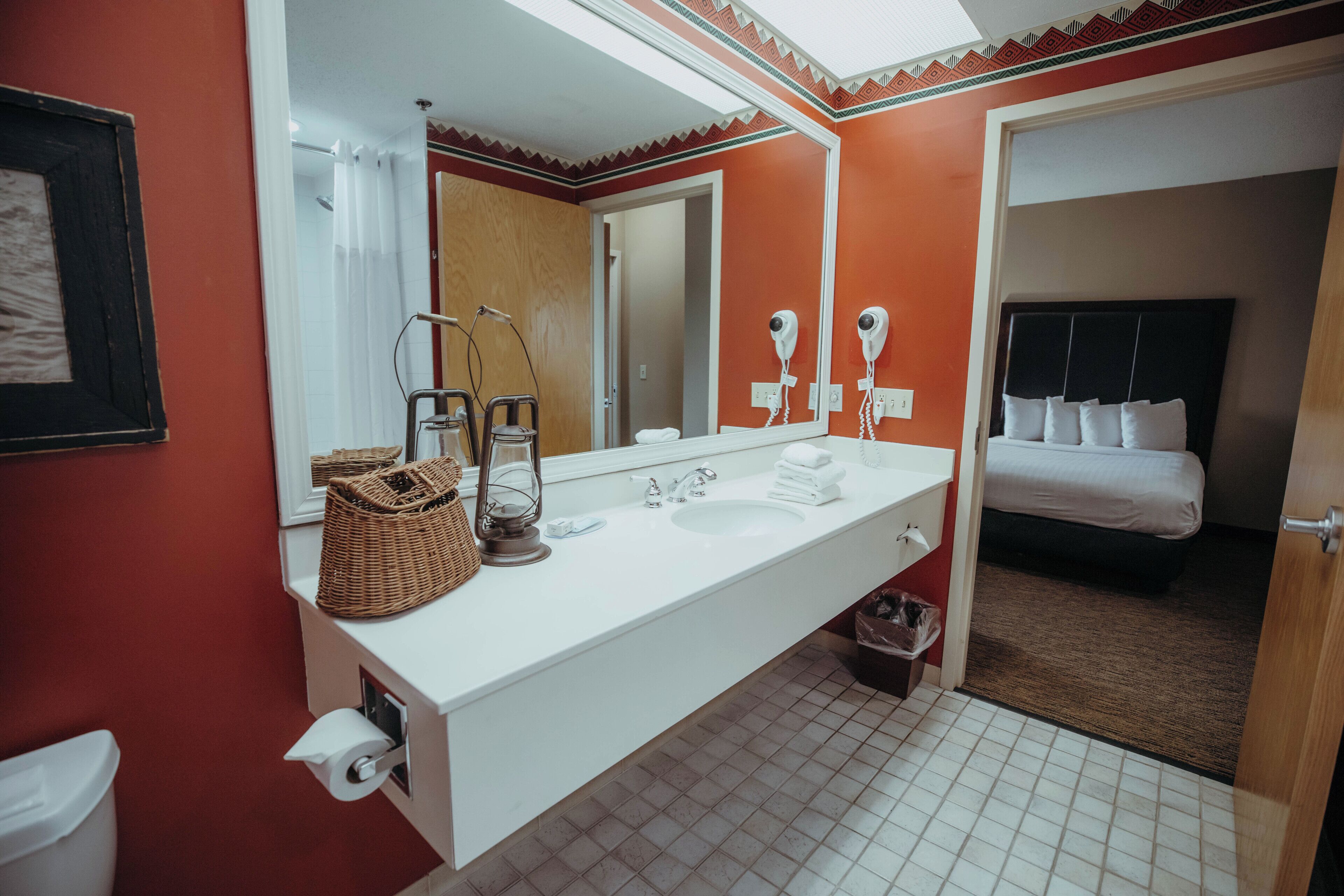 Een badkamer met een wit wastafelmeubel, een spiegel, een haardroger en een handdoekrek.