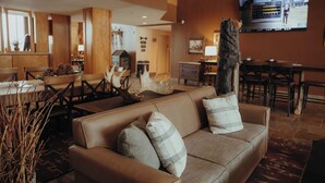 A modern lobby with a brown leather sofa, wooden dining table, and a mounted TV. - Wildwood Lodge (Pewaukee)