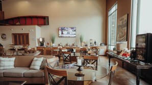 A spacious living area with a large round table, multiple chairs, a sofa, and a television mounted on the wall. - Wildwood Lodge (Pewaukee)