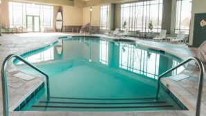 An indoor swimming pool with clear water, surrounded by lounge chairs and a stone-tiled deck. - Wildwood Lodge (Pewaukee)