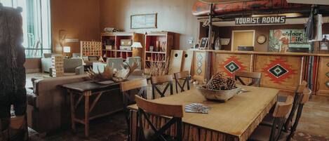 Un interno accogliente e rustico con un tavolo da pranzo in legno, sedie e un'ampia finestra. Si nota un cartello con la scritta 'Tourist Rooms' e una sveglia appesa al muro.