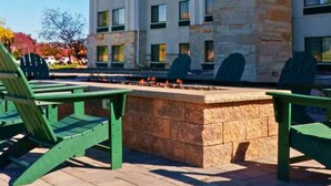 A hotel with a stone facade, multiple windows, and outdoor seating with green chairs. - Wildwood Lodge (Pewaukee)