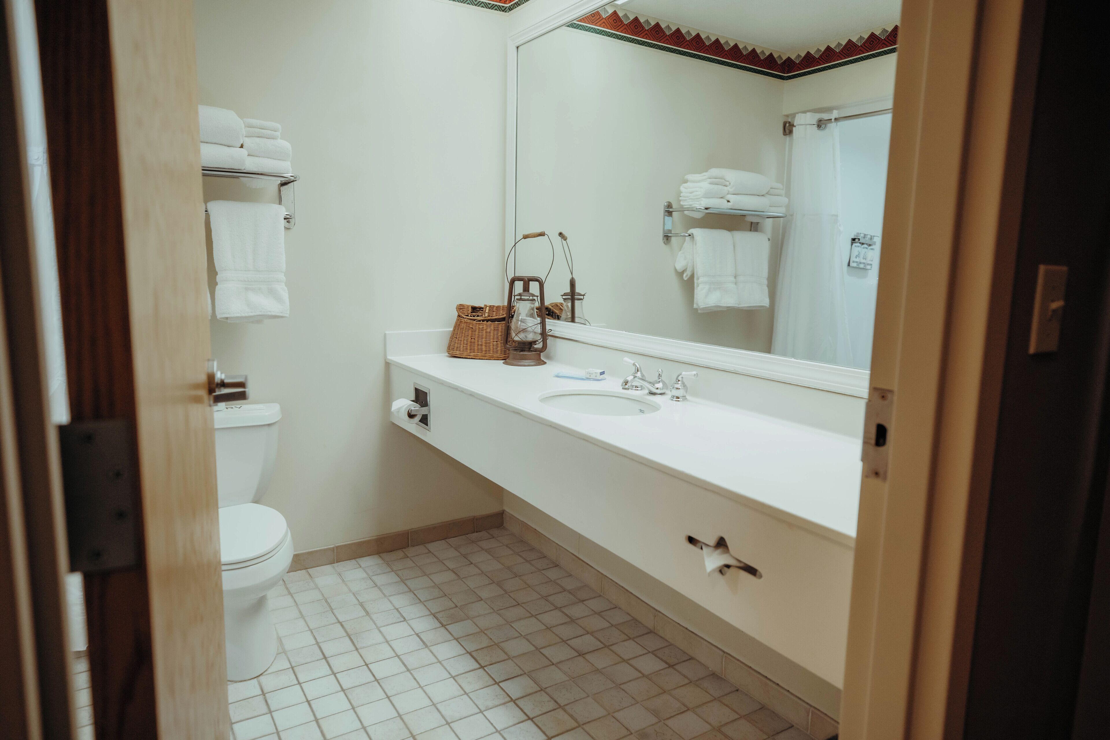 Un baño con inodoro, lavamanos con espejo y un perchero para toallas.