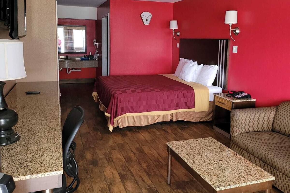 A hotel room with a bed, a desk, a chair, a small table, and a sofa.