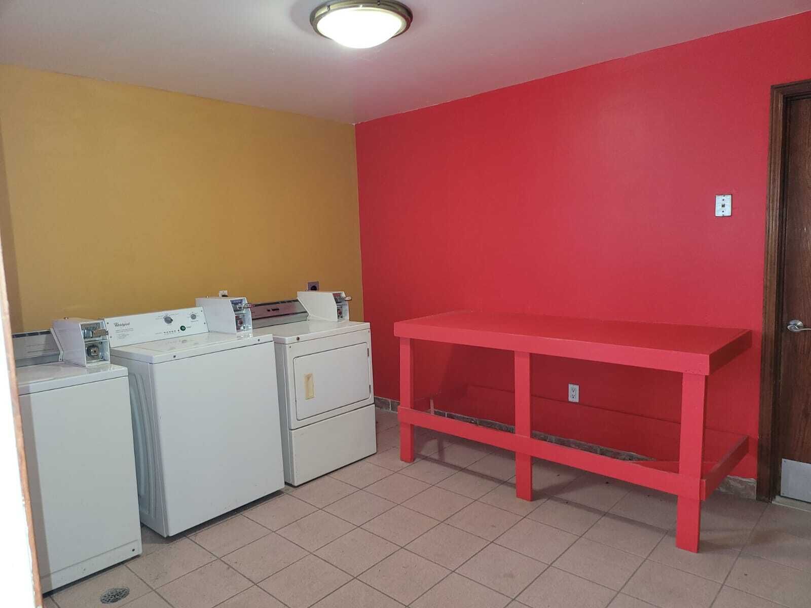 A laundry room with a red table and three white washing machines.