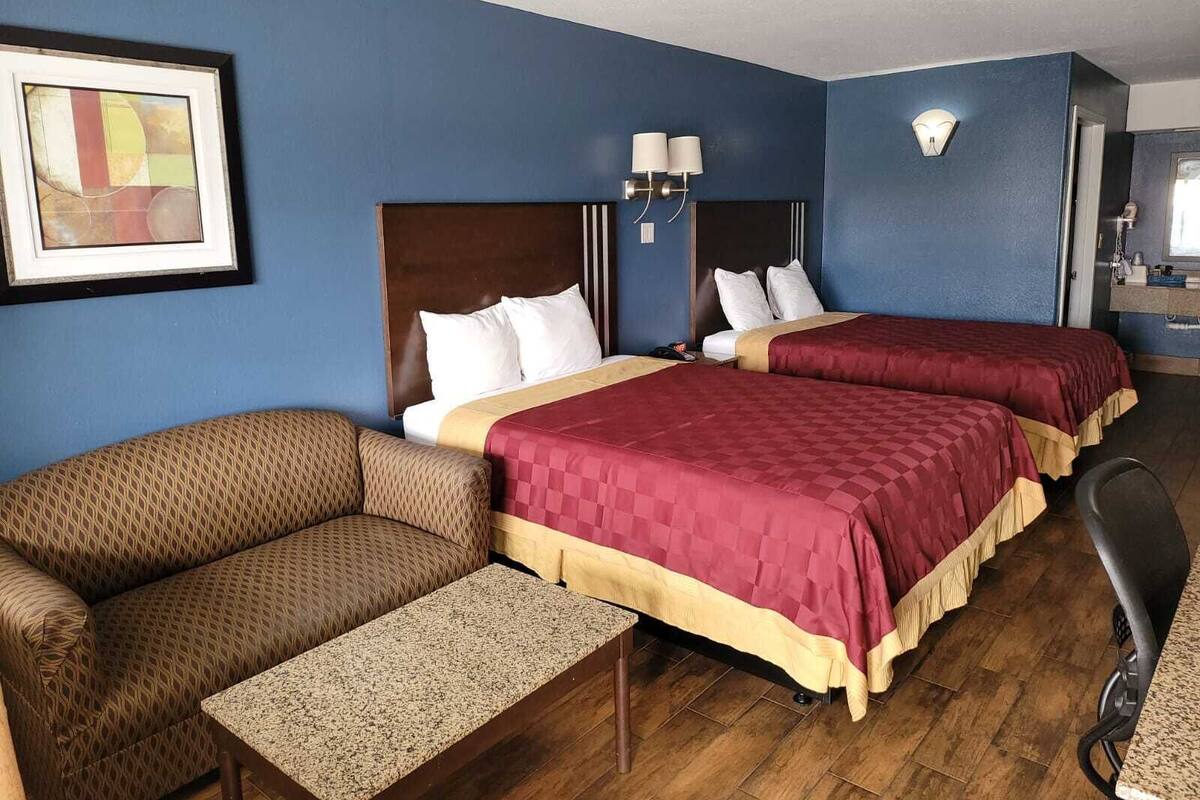 A hotel room with two beds, a sofa, a small table, and a chair.
