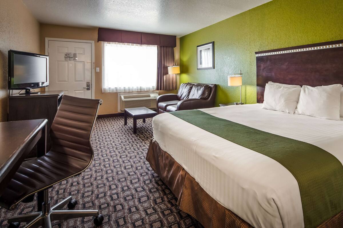 Habitación de hotel con una cama grande, un escritorio con silla, televisor, ventana con cortinas e imagen colgada en la pared.