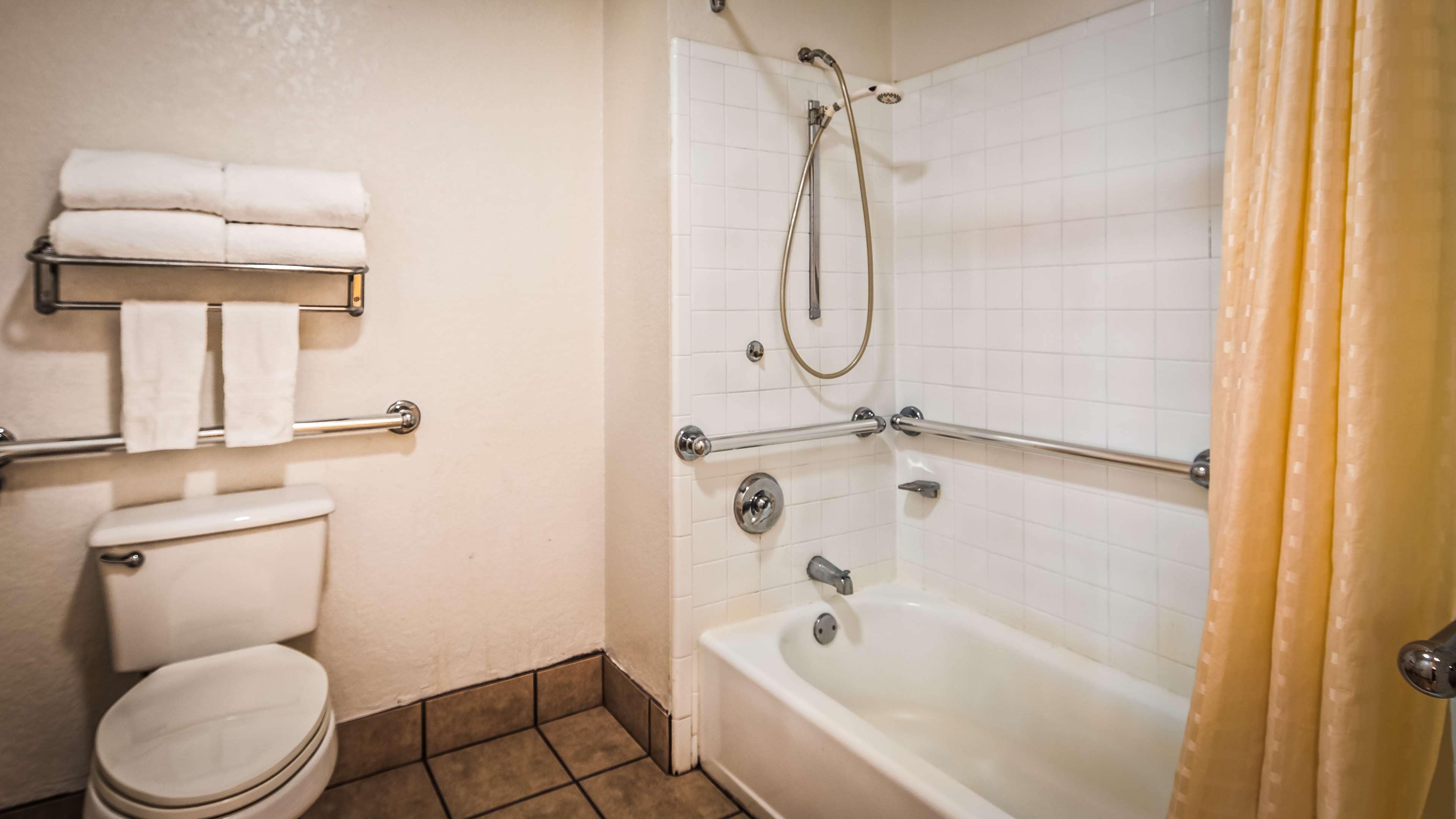 A bathroom with a toilet, a bathtub, and a shower. There are towels on a rack and a curtain on the shower.