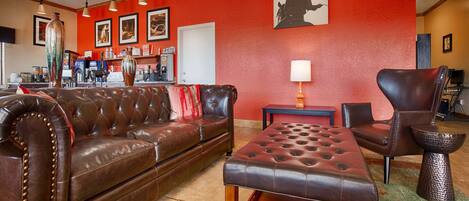Une pièce avec un canapé en cuir marron, un pouf assorti, un mur d’accent rouge et une silhouette de cowboy encadrée.