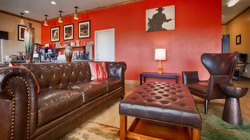 Una habitación con sofá de cuero marrón, un reposapiés a juego, una pared de acento roja y una silueta de vaquero enmarcada.