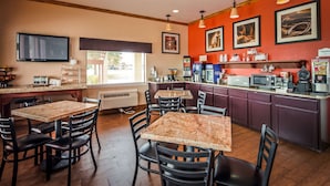 Interior de un restaurante con mesas de mármol y sillas negras, una barra de cocina con máquinas de café y cuadros en la pared.