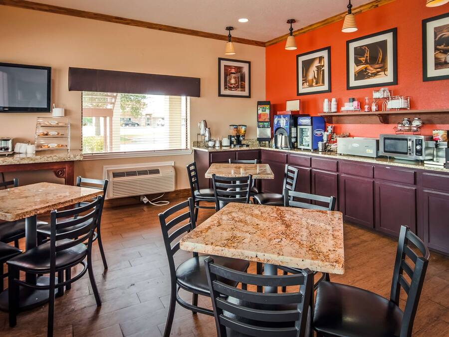Interior de un restaurante con mesas de mármol y sillas negras, una barra de cocina con máquinas de café y cuadros en la pared.
