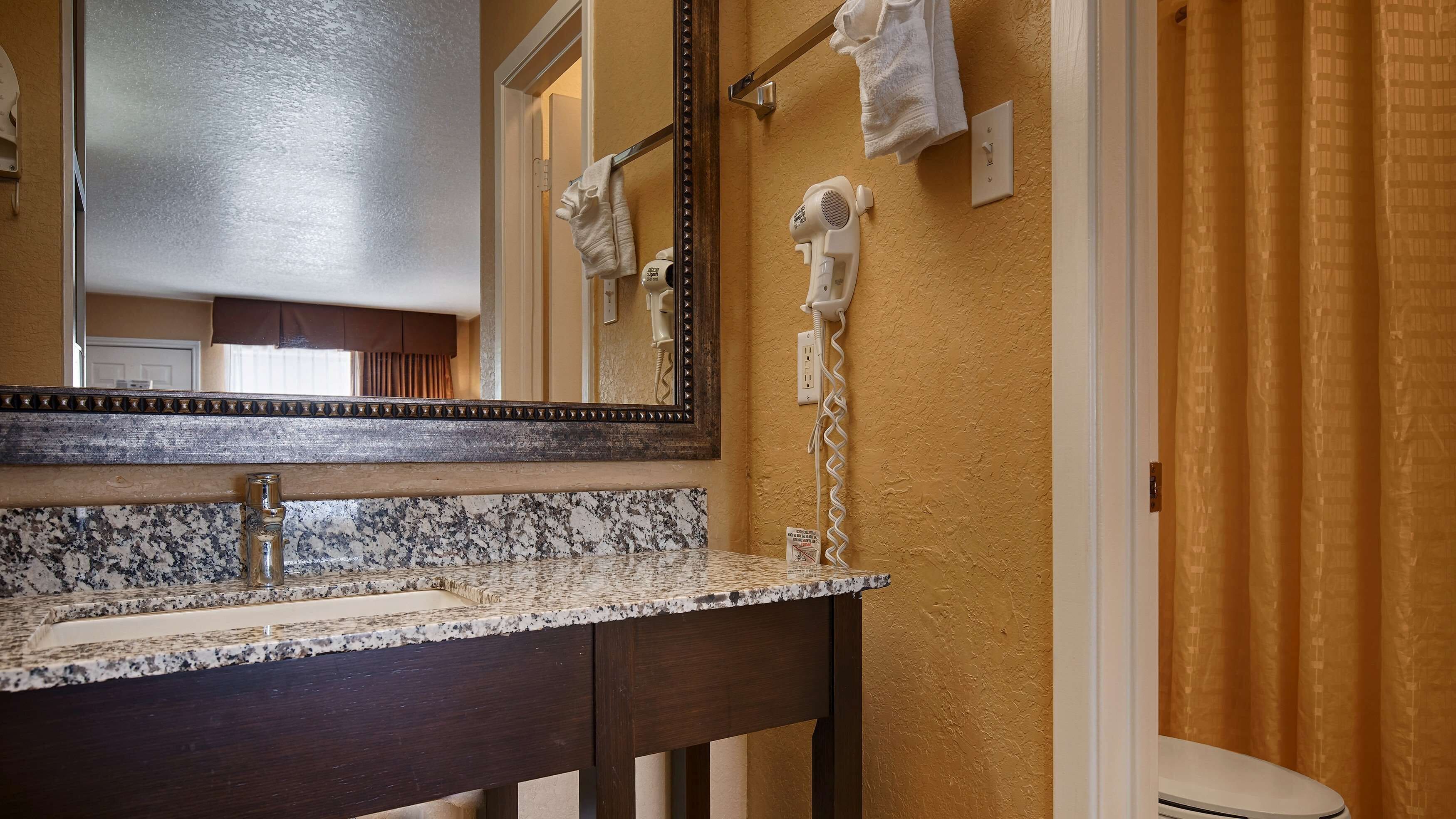 Un bagno con lavabo su piano in granito, uno specchio grande e un asciugacapelli montato a parete.