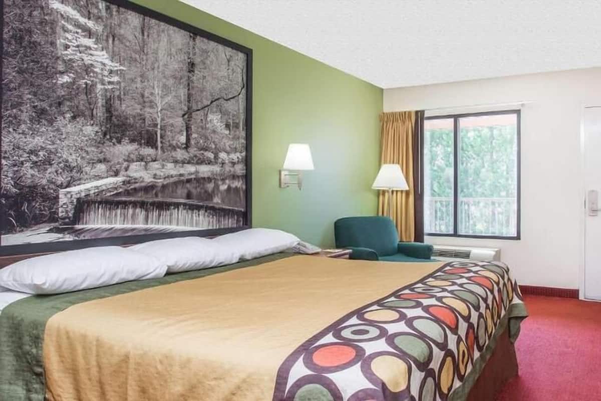 Ein Hotelzimmer mit Bett, Fernseher, einem Fenster mit Vorhängen und einem Bild an der Wand.