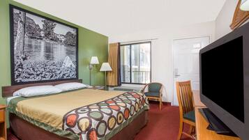 Une chambre d’hôtel avec un lit, une télévision, une chaise, un bureau, une lampe et un grand tableau au mur.