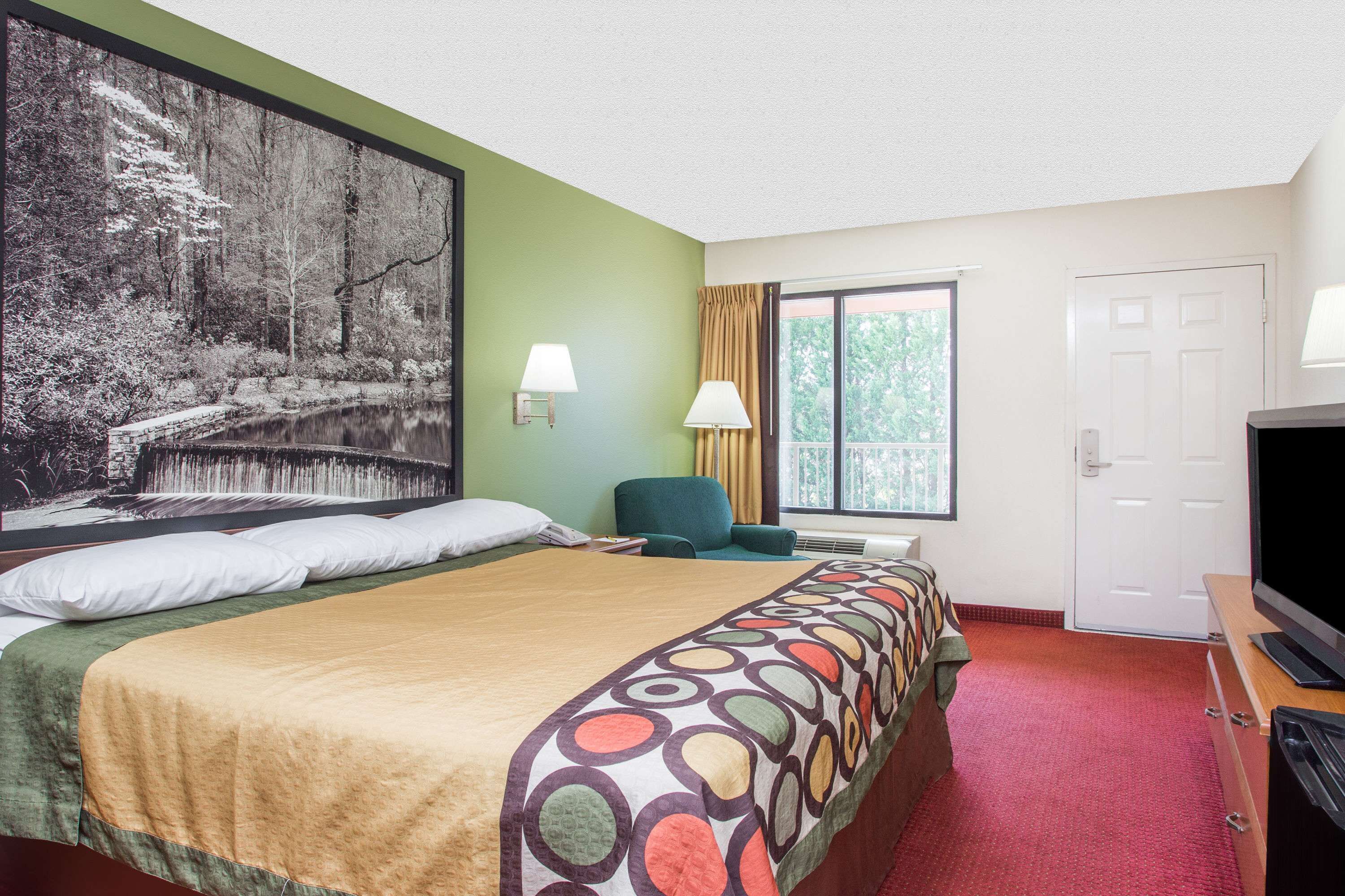A hotel room with a large bed, a television, a desk, and a window with curtains.