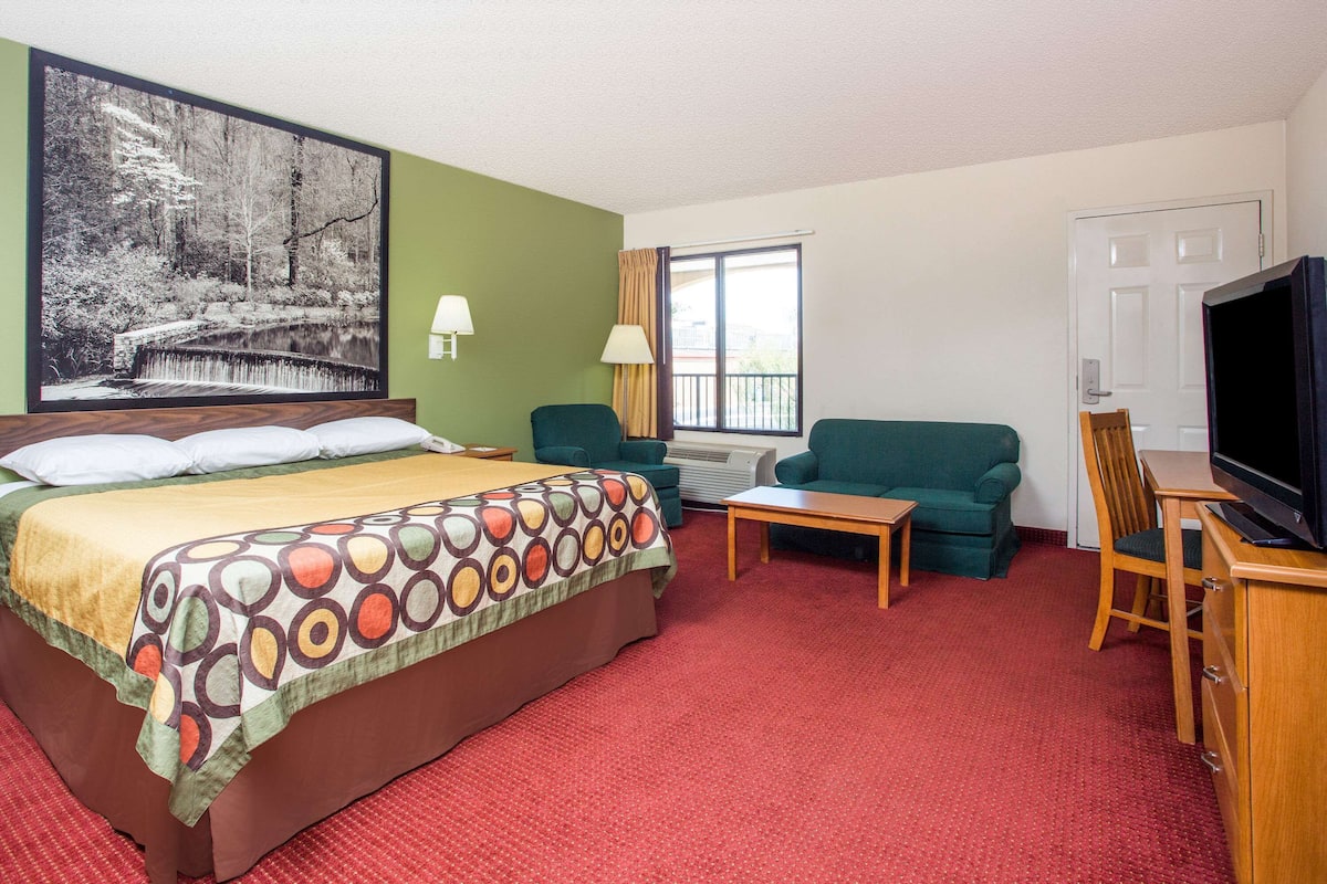 Ein Hotelzimmer mit einem Bett, einem grünen Sofa, einem kleinen Tisch, einem Fernseher und einem großen Fenster.
