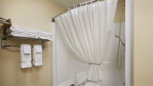 Une salle de bain avec une douche, une petite chaise blanche et un porte-serviettes avec des serviettes pliées.