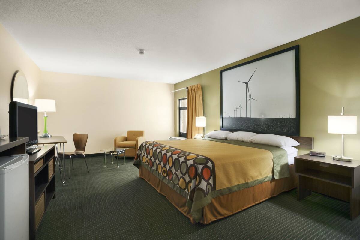 Ein Hotelzimmer mit einem Bett, einem Schreibtisch mit Computer, einem Sessel, einem Fernseher und einem Fenster mit Vorhängen.